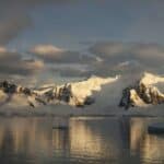 Dusk and flat calm water off the shore of a mountain landscape in Antarctica.