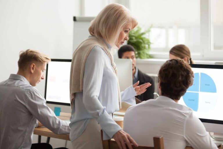 Senior female executive mentor supervising computer work of young intern